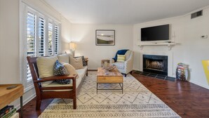 A living room with a sofa, armchair, coffee table, fireplace, TV, and a patterned rug.