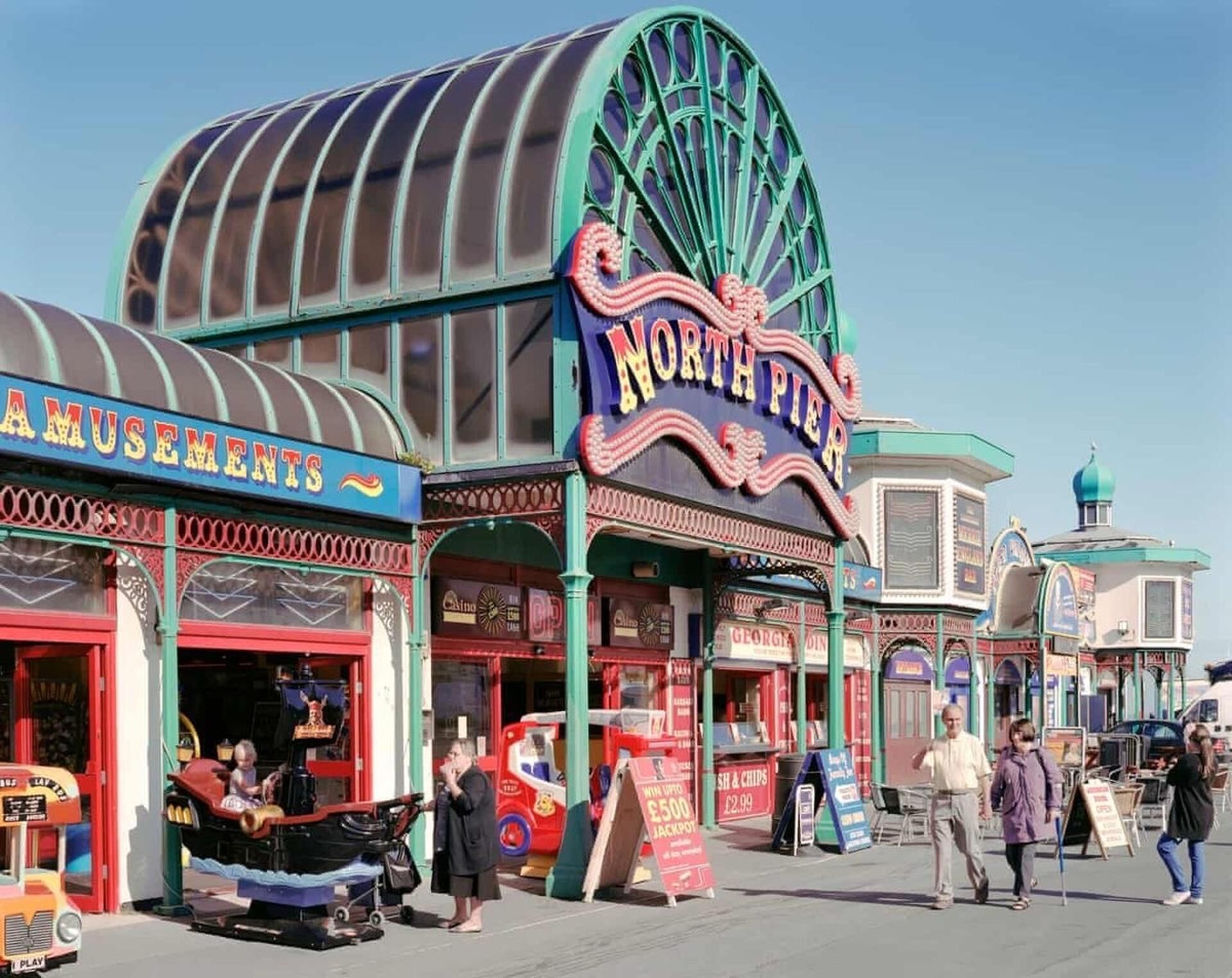 Une salle d’arcade animée, avec une grande roue bien visible et de nombreux jeux électroniques.