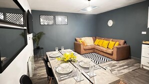 A modern living room with a sectional sofa, dining table set for four, and a decorative wall panel. - Oak Suite - 2 Bed - Sleeps 4 - Central Blackpool (Blackpool)