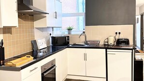 A modern kitchen with white cabinets, a black countertop, a built-in oven, a sink, and a window providing natural light. - Oak Suite - 2 Bed - Sleeps 4 - Central Blackpool (Blackpool)