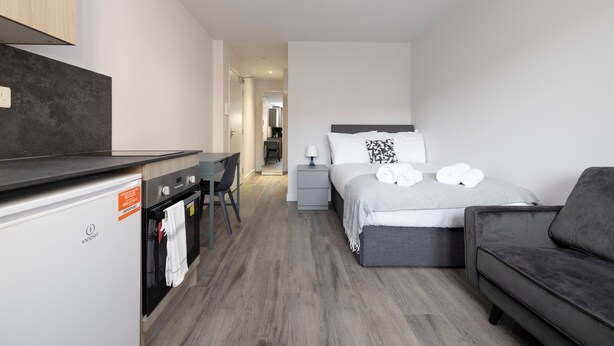 A compact hotel room with a kitchenette, a bed with pillows, a bedside table, and a sofa. - JOIVY Chic Studio near Holyrood Park (Edinburgh)