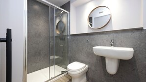 A modern bathroom with a glass-enclosed shower, a white toilet, and a wall-mounted sink. - JOIVY Chic Studio near Holyrood Park (Edinburgh)