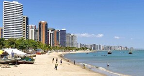 A beach with a row of high-rise buildings in the background, a sandy shore, and several boats in the water. - Conforto a Beira Mar no Golden Fortaleza (Fortaleza)