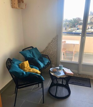 A corner room with two black wicker chairs, one with a yellow cushion, and a small round table with a book and a mug.