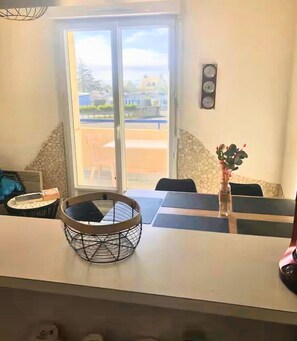 A dining area with a table, chairs, a vase with flowers, and a view through a glass door.