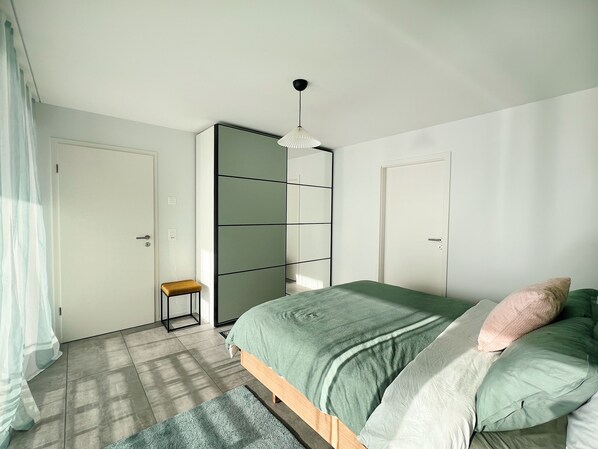 A bedroom with a bed, a small stool, a wardrobe, and a door.