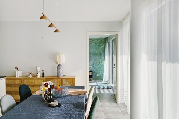 A modern dining area with a table set for two, a wooden cabinet, and a view into a room with patterned wallpaper.