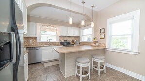 A modern kitchen with white cabinetry, a large island with bar stools, a dishwasher, and a refrigerator.