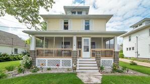 A two-story house with a front porch, a stone foundation, and a small garden with flowers and shrubs.