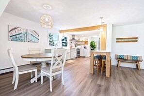 A modern kitchen with white cabinetry, a wooden dining table, and a bench. - Beachwood Getaway Sleeps 10! (Wells)
