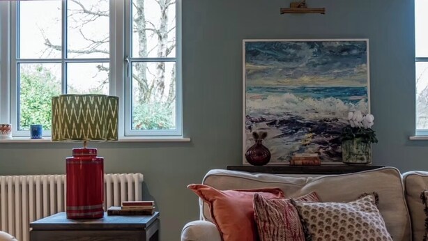 A cozy living room with a beige sofa, a small table with a red lamp, and a painting on the wall. - Large detached farmhouse in quiet Kent countryside , close to London train line (Edenbridge)