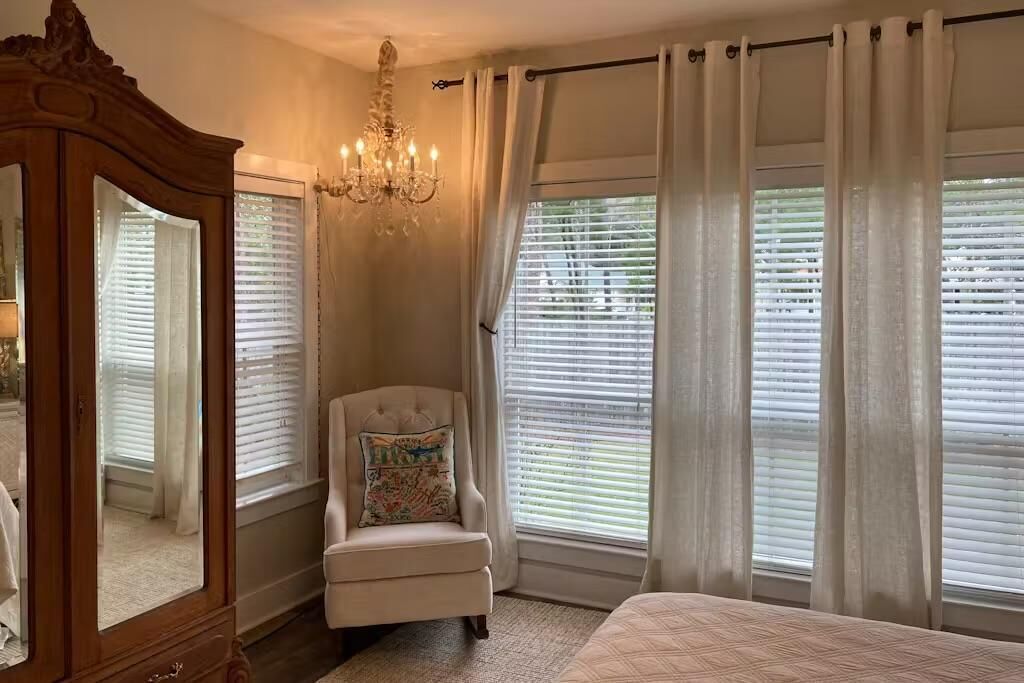 Une chambre avec un grand lit, une commode en bois, une chaise avec un coussin coloré et un lustre.