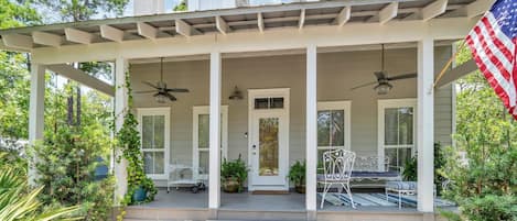 A two-story house with a covered porch, two ceiling fans, and an American flag.
