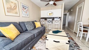 A living room with a grey sofa, yellow and patterned cushions, a coffee table, and a ceiling fan. - ⭐Walk 2 Beach-Monthly Discount-1BR Sandprints A1⭐ (Miramar Beach)