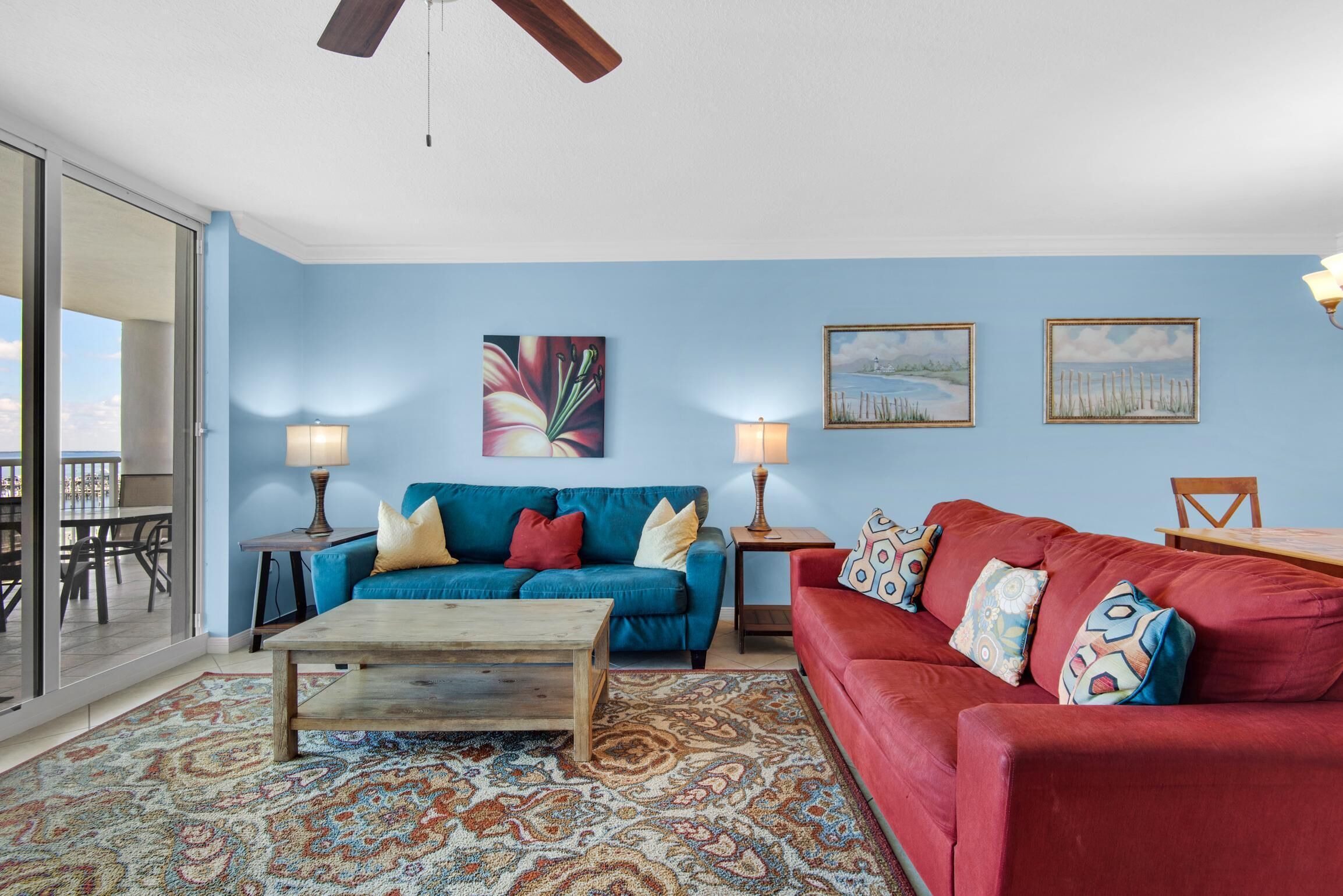 Sala de estar com parede azul, duas poltronas, uma mesa de centro e um sofá vermelho. Há duas luminárias e um quadro na parede.