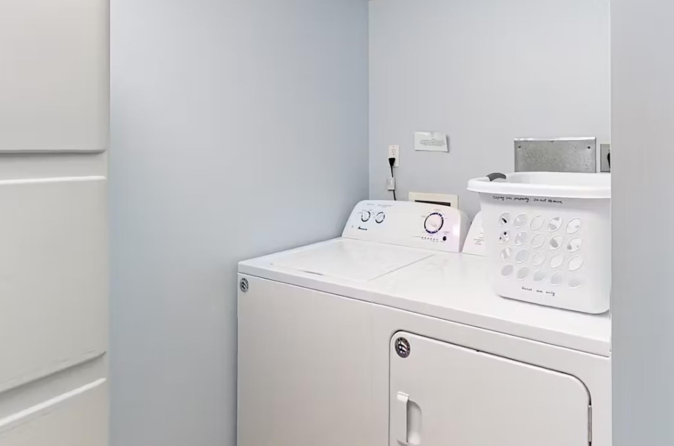 A laundry room with a front-loading washer and dryer, a wall-mounted electrical outlet, and a white utility cabinet.