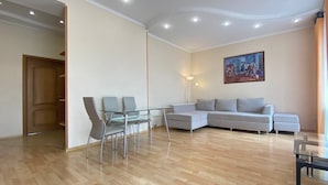 A modern living room with a glass dining table, grey sofa, and a painting on the wall.