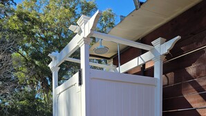 A white outdoor structure with a roof and a door, adjacent to a wooden fence.