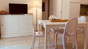 A small, modern kitchen with white cabinets, a dining table with chairs, a television on a cabinet, and a lamp. - Dimora Agnese Deluxe Apartment (Lecce)