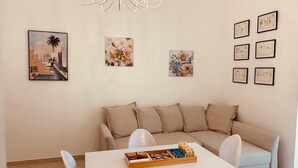 Una sala de estar con un sofá blanco, una mesa de comedor con una bandeja de pasteles y varias obras de arte enmarcadas en las paredes.
