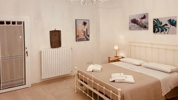 A bedroom with a bed, a radiator, a hanging towel, a chandelier, and two wall-mounted paintings. - Dimora Agnese Deluxe Apartment (Lecce)
