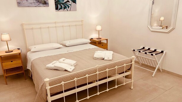 Un dormitorio ordenado con una cama, dos mesitas de noche, una mesita auxiliar, un espejo y un perchero para toallas.
