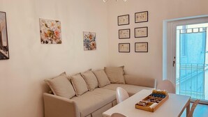 A cozy living room with a beige sofa, a white dining table, and a chandelier. There are six framed pictures on the wall. - Dimora Agnese Deluxe Apartment (Lecce)