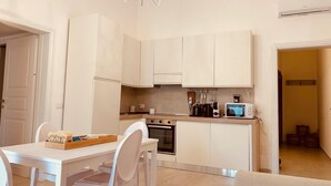 A compact kitchen with white cabinetry, a dining table with chairs, a microwave, and a chandelier. - Dimora Agnese Deluxe Apartment (Lecce)