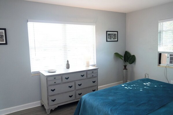 Un dormitorio con cama, cómoda, ventana con persianas y planta en maceta.