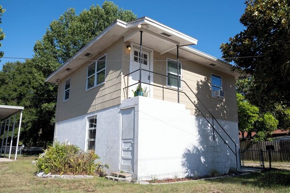 A two-story house with a flat roof, a covered porch, and a small garden area.