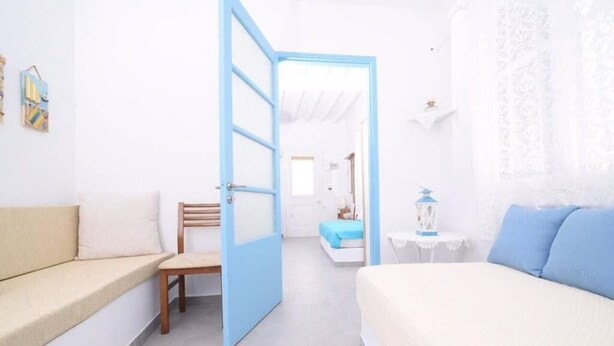 A room with a bed, a chair, a sofa, and an open door leading to another room. - Old Town Traditional House (Paros)