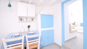 A dining area with a table set for two, a white cabinet with blue doors, and a view of a balcony with a white sofa. - Old Town Traditional House (Paros)