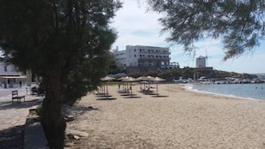 A beach with a row of umbrellas, a building in the background, and a windmill. - Old Town Traditional House (Paros)
