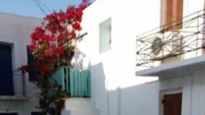 A white building with a stone-paved courtyard, a staircase, and a red flower arrangement. - Old Town Traditional House (Paros)