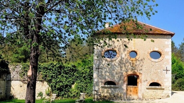 A stone building with a tiled roof, circular windows, and a door. - Domaine du Ris de Feu (Chalais)