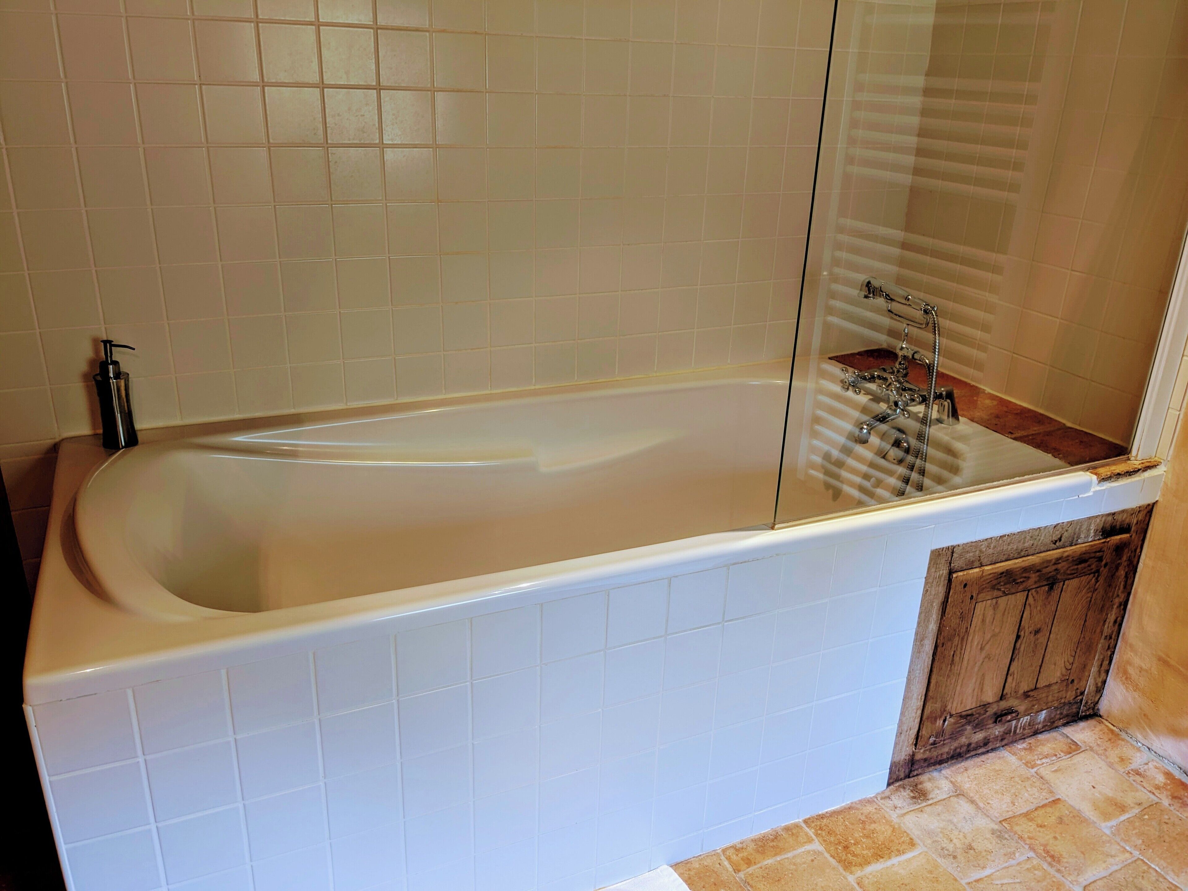 A bathroom with a bathtub, a glass shower enclosure, and a wooden door.