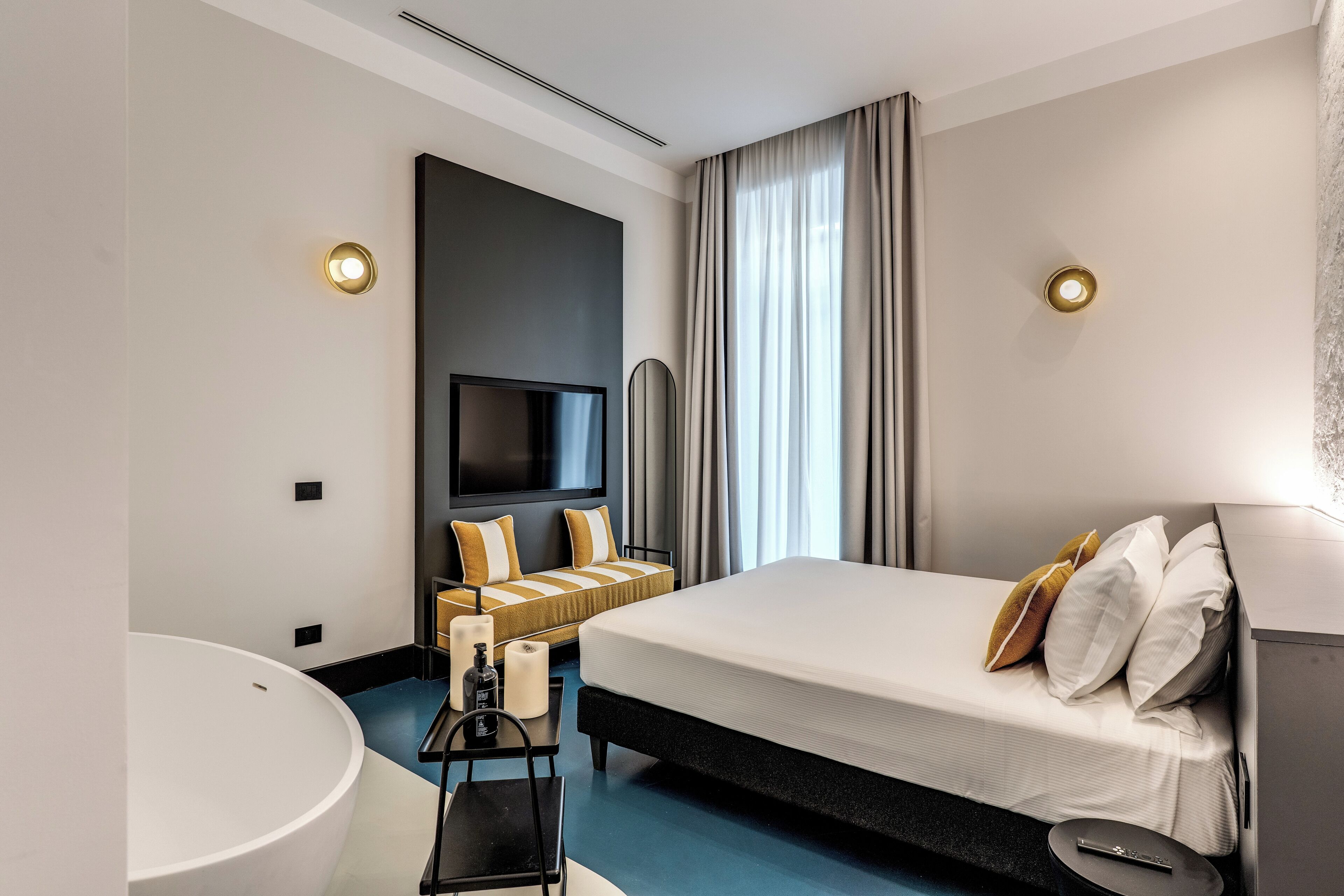 Une chambre d’hôtel moderne dotée d’un grand lit, d’un téléviseur à écran plat, d’un canapé, d’un lavabo rond dans la salle de bain et d’une grande fenêtre avec des rideaux.