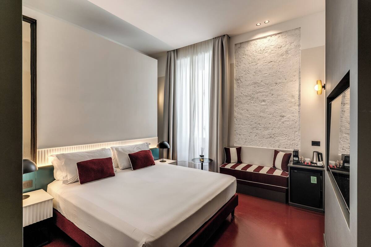 A hotel room with a large bed, bedside tables, a small desk, a chair, and a minibar.