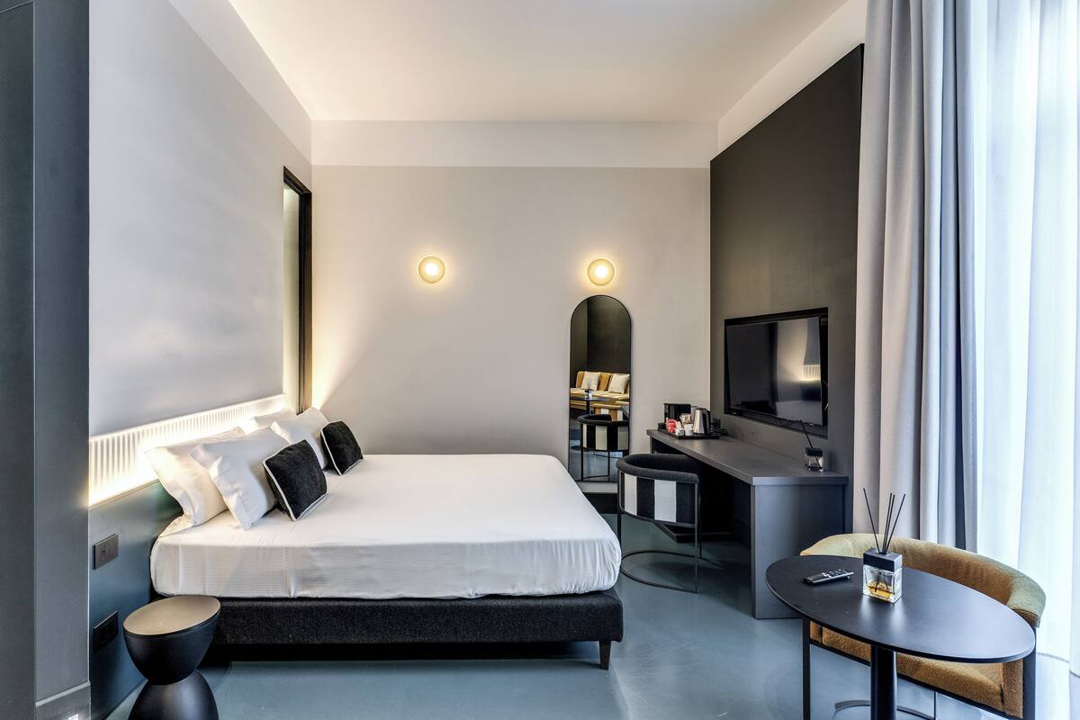 A modern hotel room with a large bed, a desk, a television, and a view of the city.