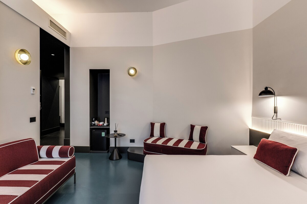 Een hotelkamer met een bed, twee slaapbanken, een kleine tafel en een spiegel.