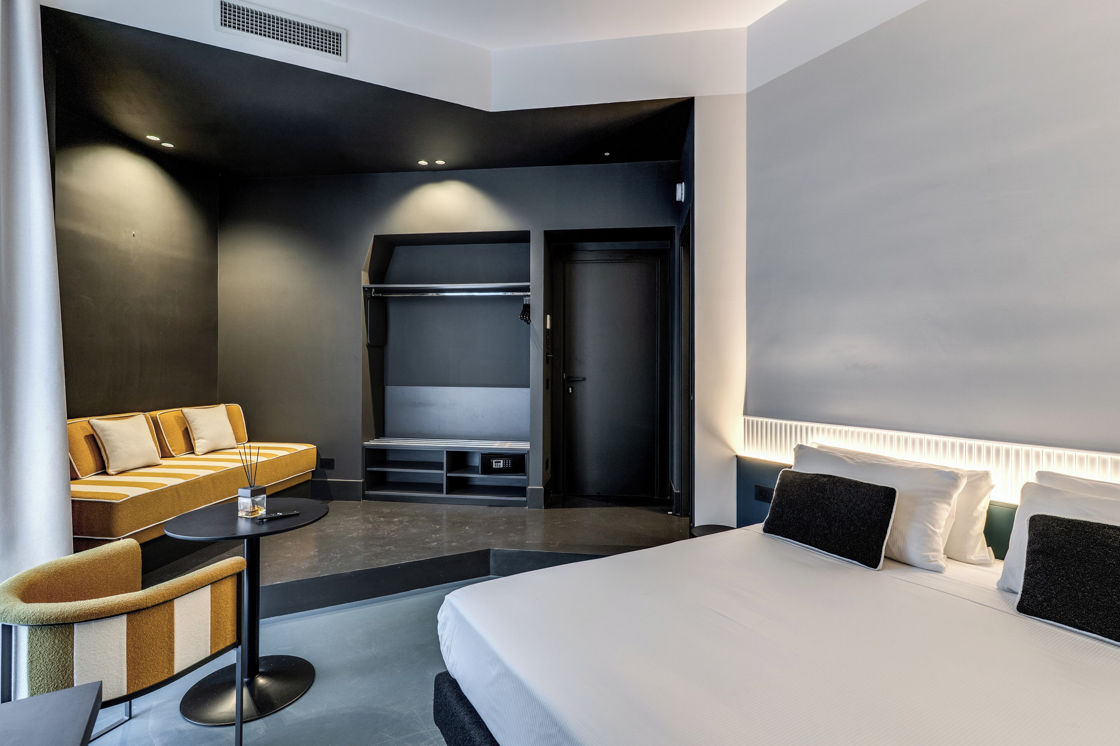 A modern hotel room with a bed, a sofa, a desk, and a walk-in closet.