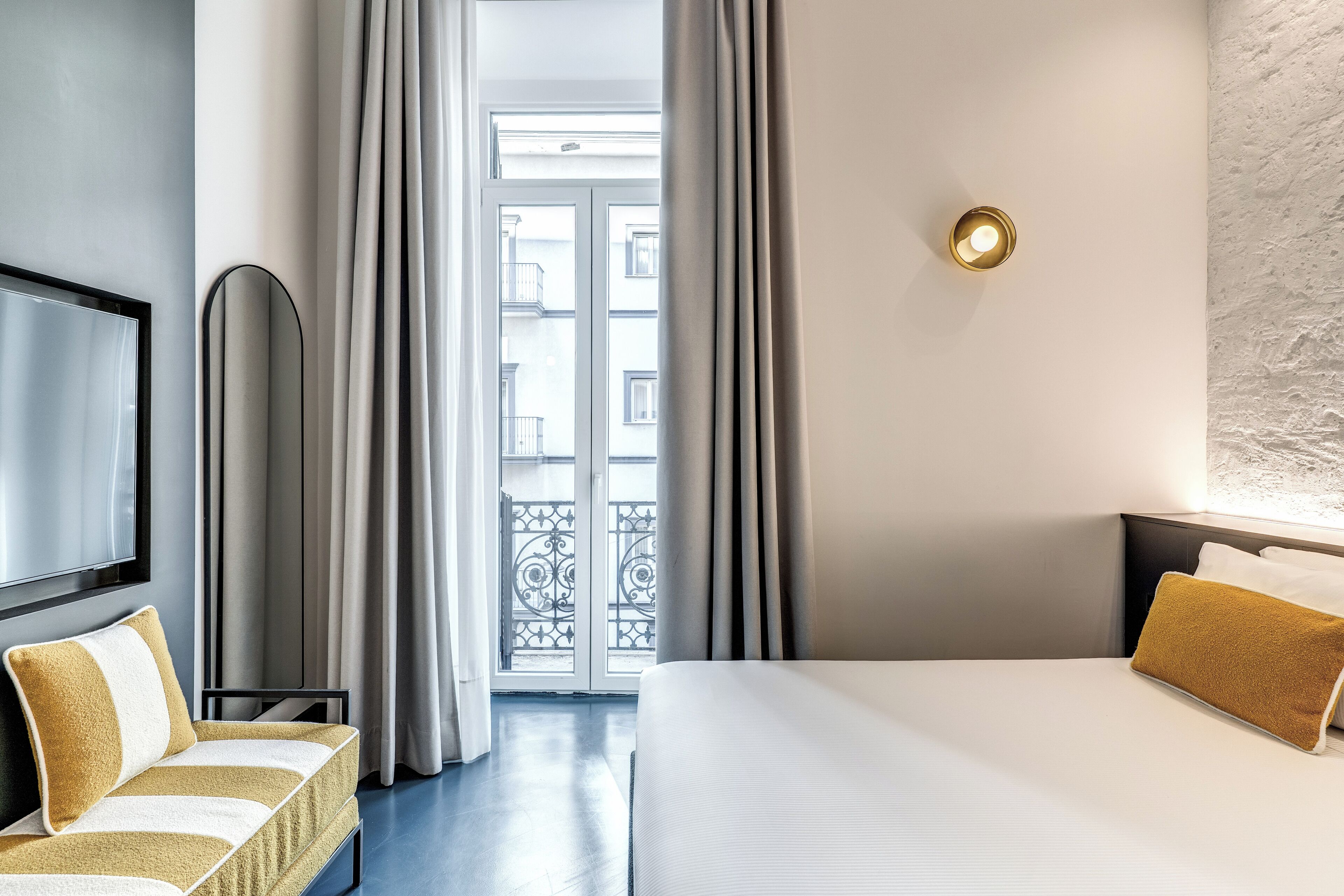 A hotel room with a bed, a TV, a sofa, and a view of the outside balcony.