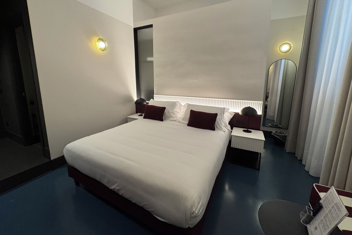A hotel room with a large bed, bedside tables, a floor lamp, and a mirror.