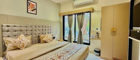 A bedroom with a large bed, a ceiling fan, an air conditioning unit, a window with curtains, and a wardrobe.