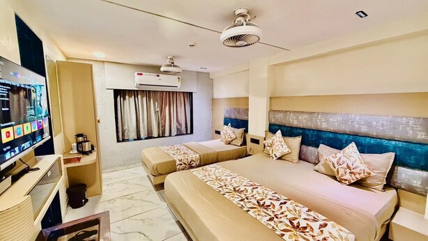 A hotel room with two beds, a TV, a desk, and a ceiling fan. - Hotel RV Residency (Ahmedabad)