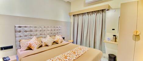 A hotel room with a large bed, a bedside table with a phone, a wardrobe, and an air conditioning unit.