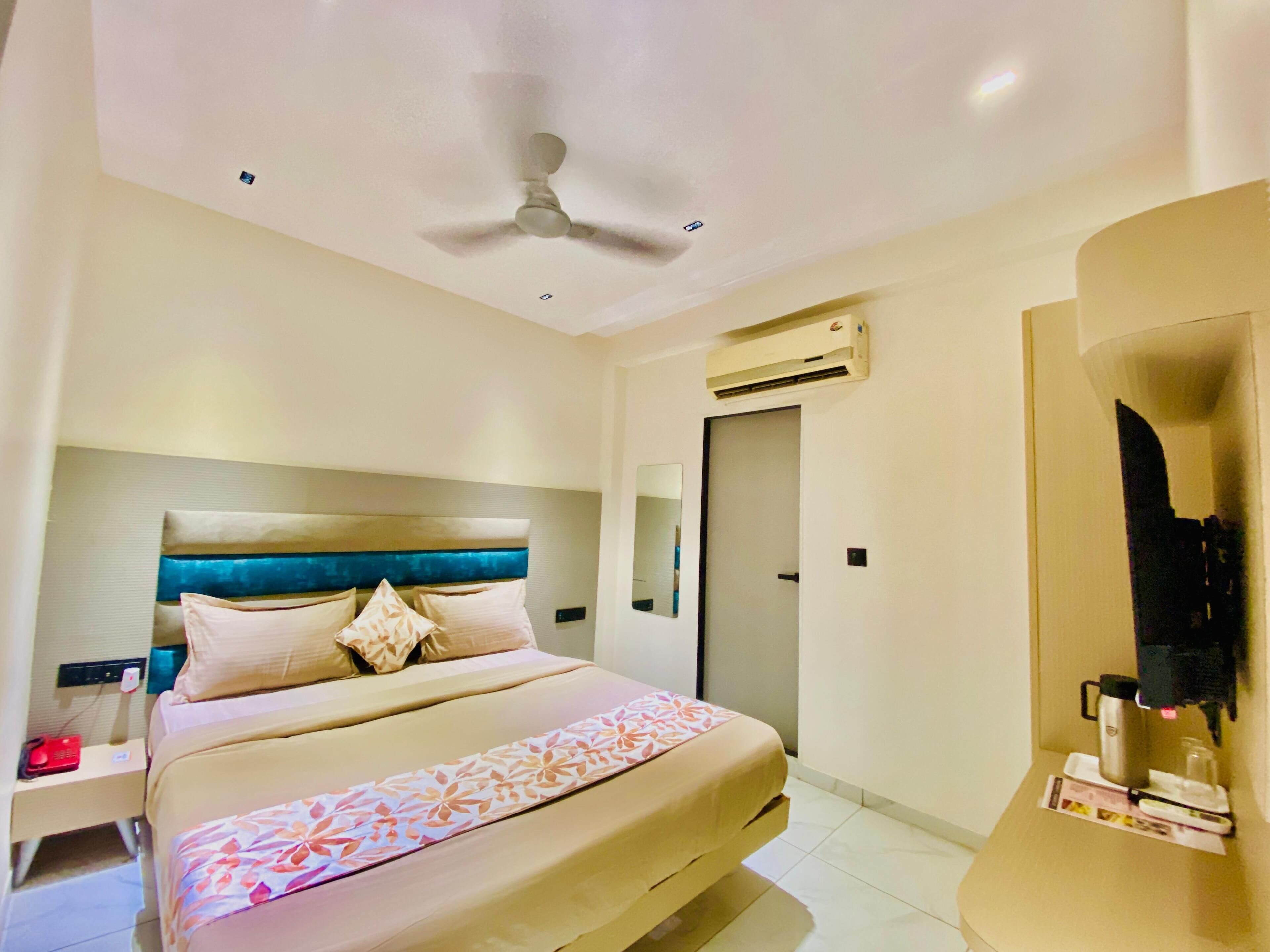 A hotel room with a bed, a nightstand, a ceiling fan, an air conditioning unit, and a mirror.