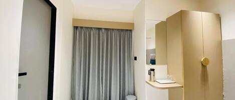 A modern hotel room with a large wardrobe, a small vanity with a mirror, and a curtain.