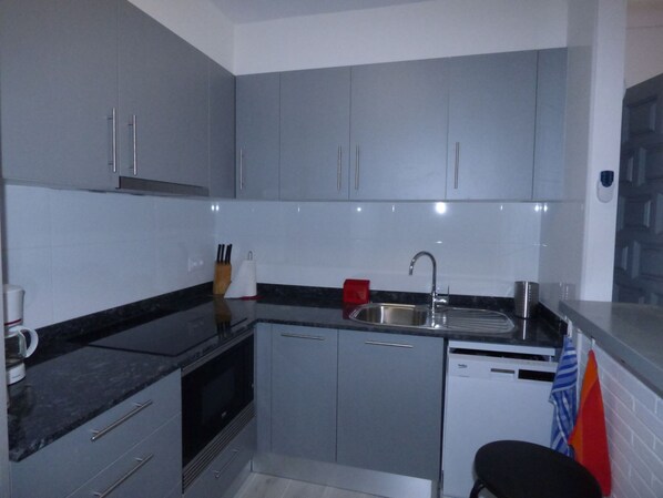 A compact kitchen with grey cabinets, a stainless steel sink, and a dishwasher.