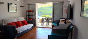 A living room with a sofa, a TV, and a balcony with a table and chairs.
